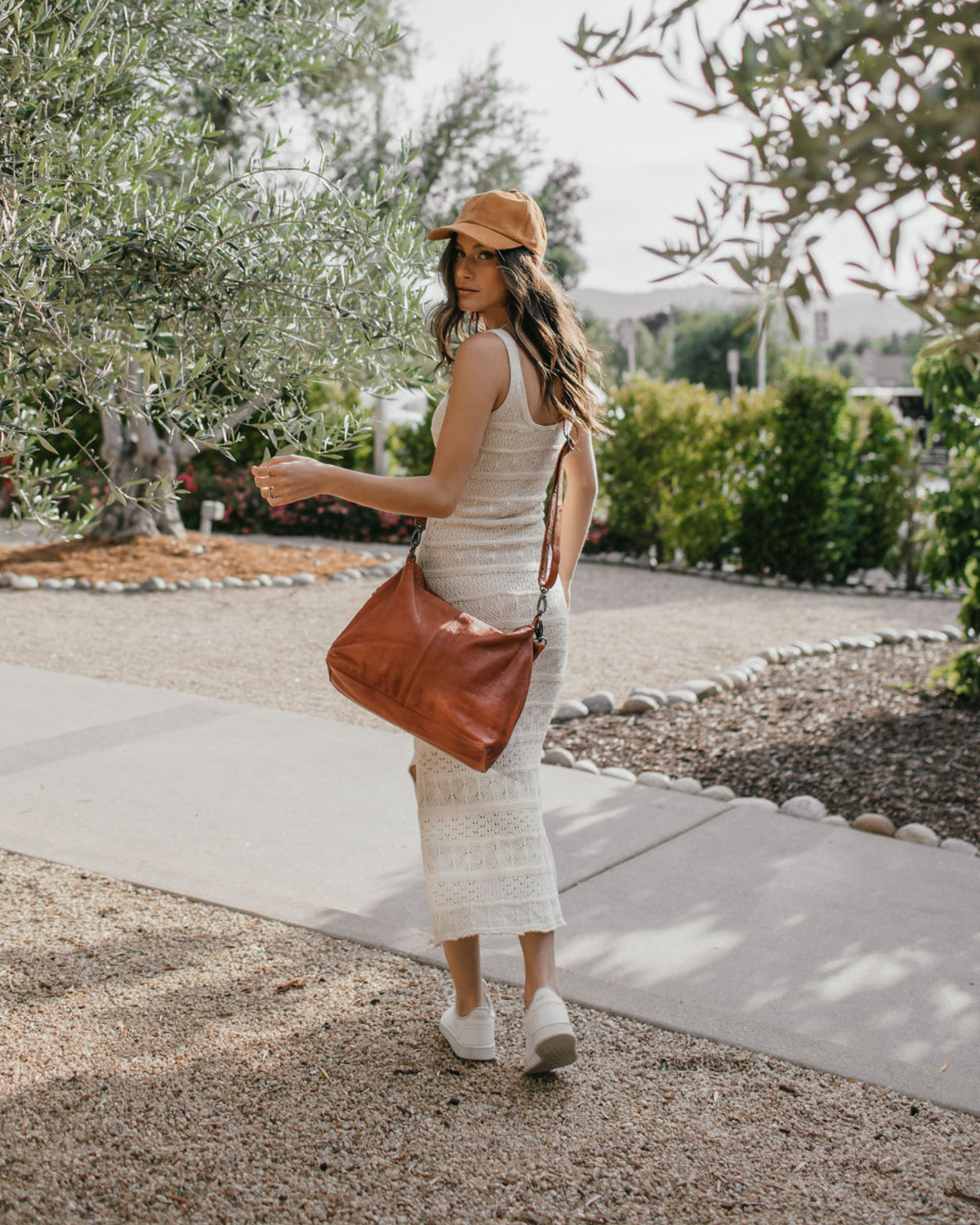 White midi dress, brown purse, and brown cap from Roux Collective Boutique.