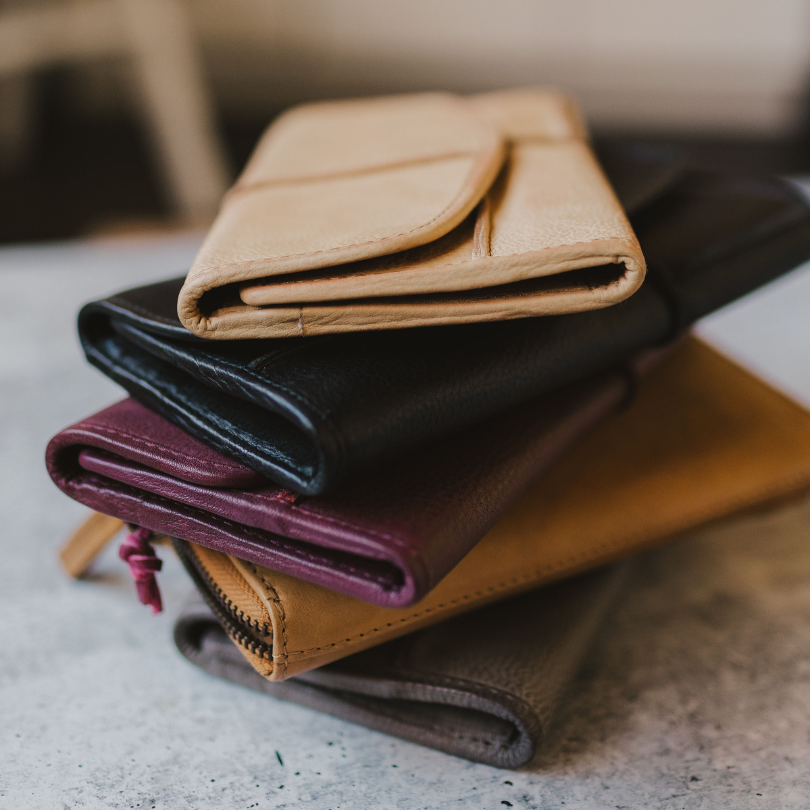 Roux Collective Boutique leather wallets in tan, black, and purple.
